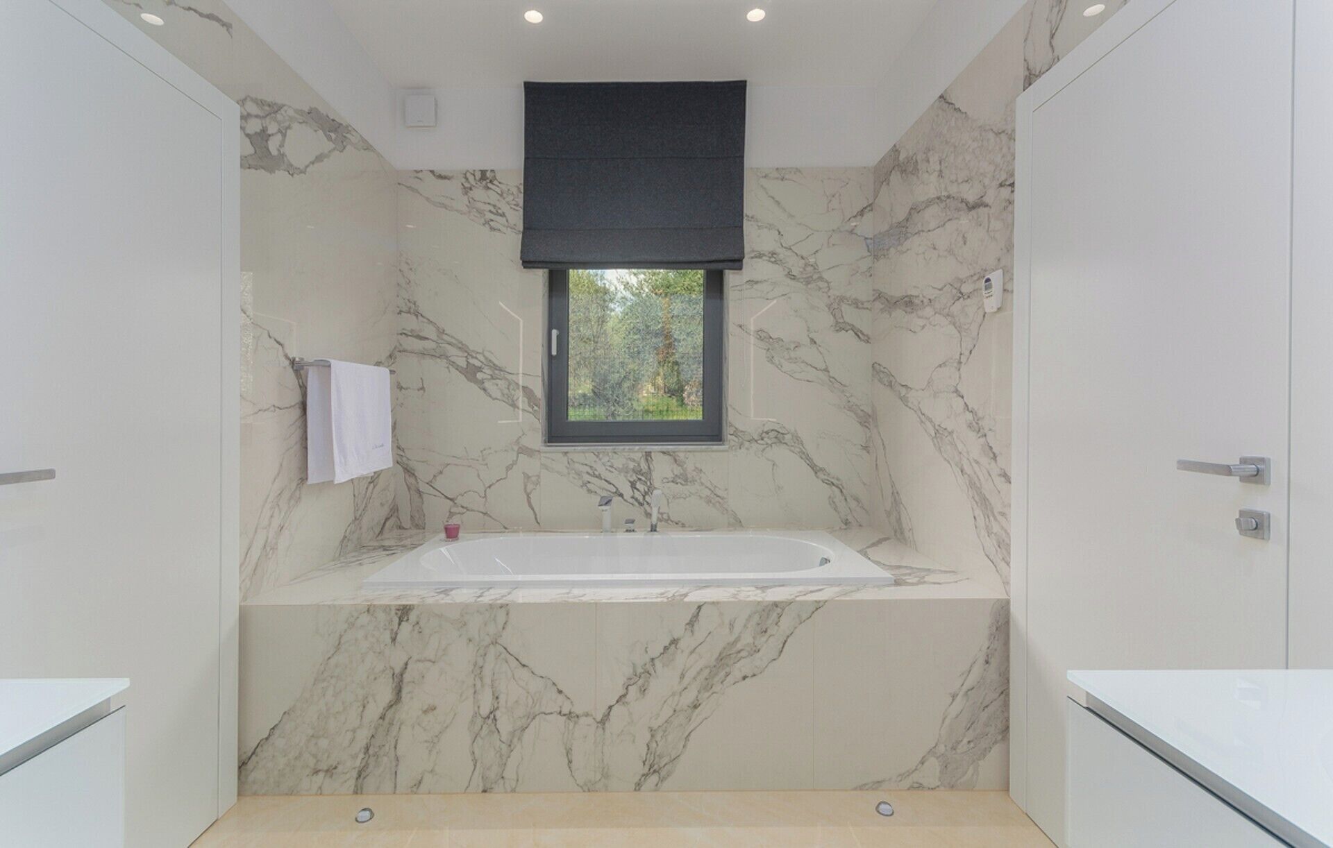 Ein modernes Badezimmer mit Marmorwand, einem Fenster und einer Badewanne.