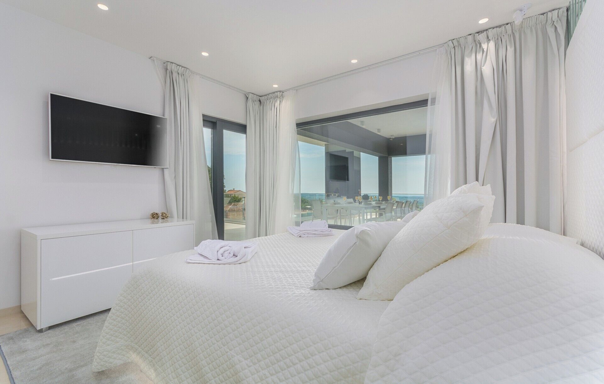 Een moderne slaapkamer met een groot bed, een tv aan de muur en een balkon met een glazen deur.