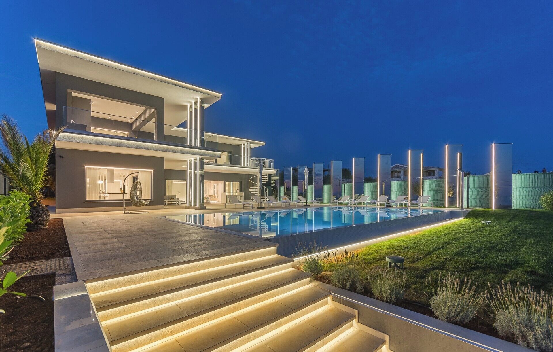 Uma casa moderna de dois andares com piscina, área de estar externa e escadaria bem iluminada.