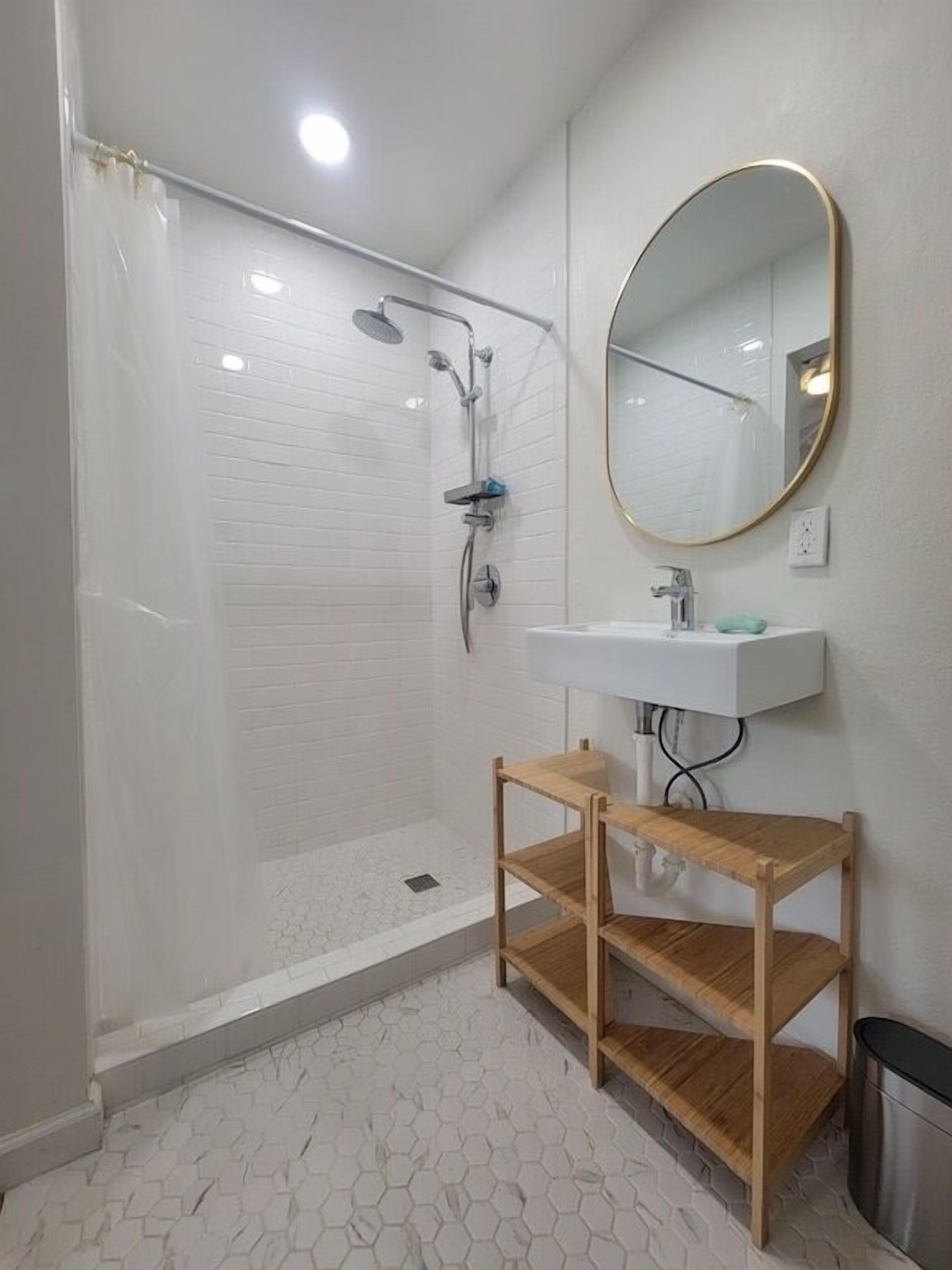 A modern bathroom with a glass-enclosed shower, a white sink with a mirror, and a wooden shelf.