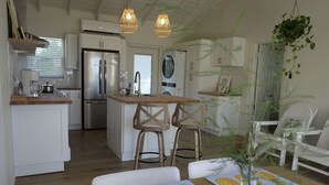 A modern kitchen with white cabinets, stainless steel appliances, and wooden bar stools. - NEW 2 bdrm Sunrise Villa on 1+ acre tropical garden directly on Hoopers Beach (George Town)