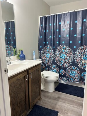 Une salle de bain avec un lavabo blanc, des meubles en bois, des toilettes et un rideau de douche à motifs floraux.