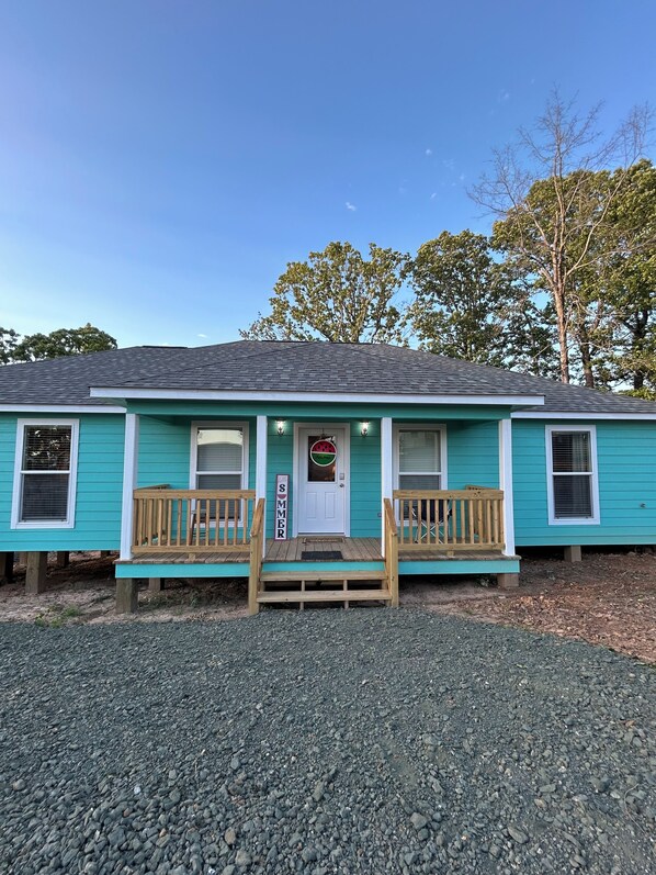 Une maison turquoise de plain-pied, dotée d’un porche à l’avant, d’une pancarte de bienvenue et d’une petite boîte aux lettres.