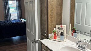 Un baño moderno con un lavamanos blanco, armarios de madera oscura y un espejo grande.
