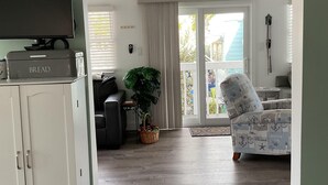 A living room with a television, a cabinet, a plant, a chair, and a view through a glass door to the outside. - Bimini Breeze - VO 313 (Cudjoe key)