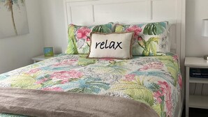A bed with a floral bedspread, a 'relax' pillow, and a nightstand with a lamp. - Bimini Breeze - VO 313 (Cudjoe key)