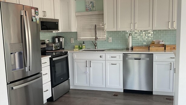 A modern kitchen with white cabinets, stainless steel appliances, a microwave, and a ceiling fan. - Bimini Breeze - VO 313 (Cudjoe key)
