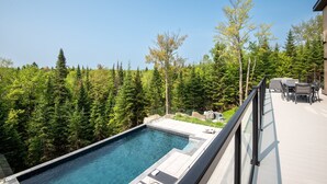 A rooftop pool with a clear view of a forested area, outdoor furniture, and a modern architectural design.