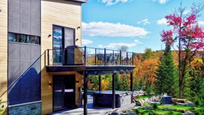 A modern two-story building with a balcony, large windows, and a view of autumn trees.
