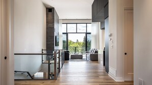 A spacious hallway with a wooden floor, a glass railing, and a view of a balcony with outdoor scenery.