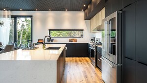 A modern kitchen with a large island, dark cabinetry, and stainless steel appliances.