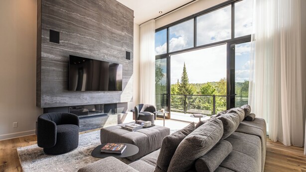A modern living room with a large TV, comfortable seating, and a balcony with a scenic view.