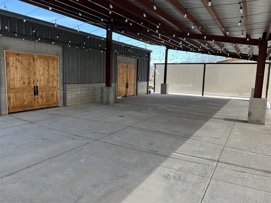 A covered outdoor area with two large wooden doors, a concrete floor, and a metal roof structure.