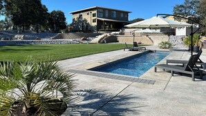 Una piscina con sillones de descanso, un patio y un edificio con fachada de piedra.
