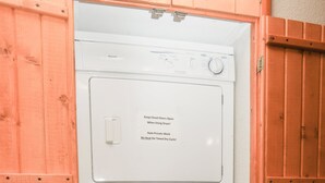 A compact, built-in laundry room with a top-loading washer and a front-loading dryer, enclosed by wooden paneling. - Walk to Downtown from Spacious Home with Hot Tub #3383 (Estes Park)