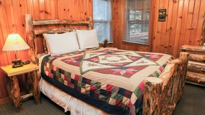 A wooden cabin bedroom with a bed, a nightstand, and a lamp. - Walk to Downtown from Spacious Home with Hot Tub #3383 (Estes Park)