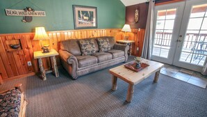 A cozy living room with a leather sofa, two side tables with lamps, a wooden coffee table, and a large window with a view. - Walk to Downtown from Spacious Home with Hot Tub #3383 (Estes Park)