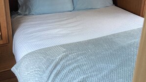 A compact bed with a white and light blue quilt in a wooden cabin-style room. - Relaxation, Privacy, Hot Tub, Pet Friendly- Kouchibouguac (Kouchibouguac)