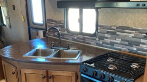 A compact kitchen with wooden cabinets, a stainless steel sink, a gas stove, and a window providing natural light. - Relaxation, Privacy, Hot Tub, Pet Friendly- Kouchibouguac (Kouchibouguac)