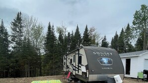 A SuperLite RV with a covered patio area, a small deck, and a tent in the background. - Relaxation, Privacy, Hot Tub, Pet Friendly- Kouchibouguac (Kouchibouguac)