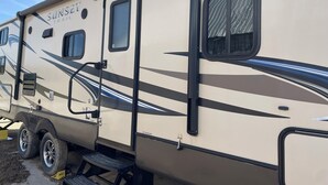 A recreational vehicle with a "Sunset Trail" label, a sliding door, and a window with a mesh screen. - Relaxation, Privacy, Hot Tub, Pet Friendly- Kouchibouguac (Kouchibouguac)