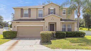 A two-story house with a beige exterior, a garage, and a well-maintained lawn.