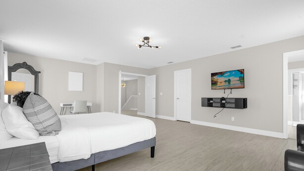 A spacious bedroom with a large bed, a desk, a chair, a TV, and a painting on the wall.
