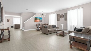 A spacious living room with a high ceiling, a dining area with a glass table, and a staircase leading to another level.