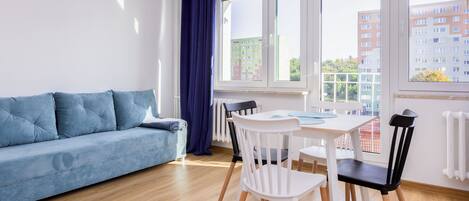 A modern living room with a sofa, dining table, chairs, and large windows.