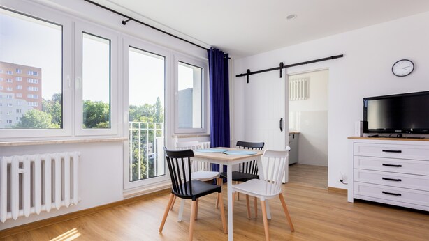 Una habitación moderna con una mesa de comedor, sillas, un televisor y ventanas amplias.