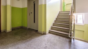 Un pasillo con una decoración en tonos verde y blanco, una puerta y una escalera con barandillas de metal.