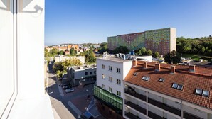 Un edificio de varios pisos con tejado de tejas rojas, diseño moderno y vistas de un paisaje urbano con diversos edificios y un cielo azul despejado.