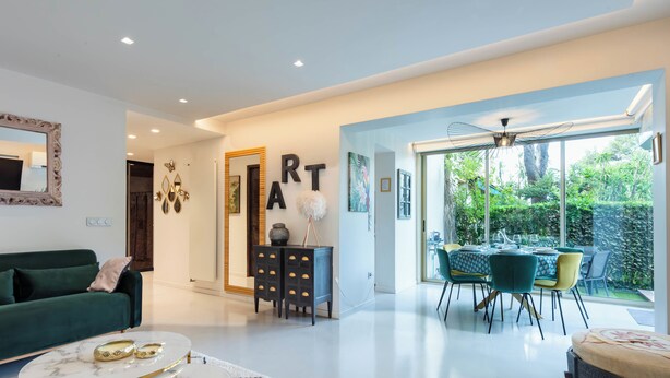 A modern living room with a green sofa, a marble coffee table, and a dining area with a glass table and chairs.