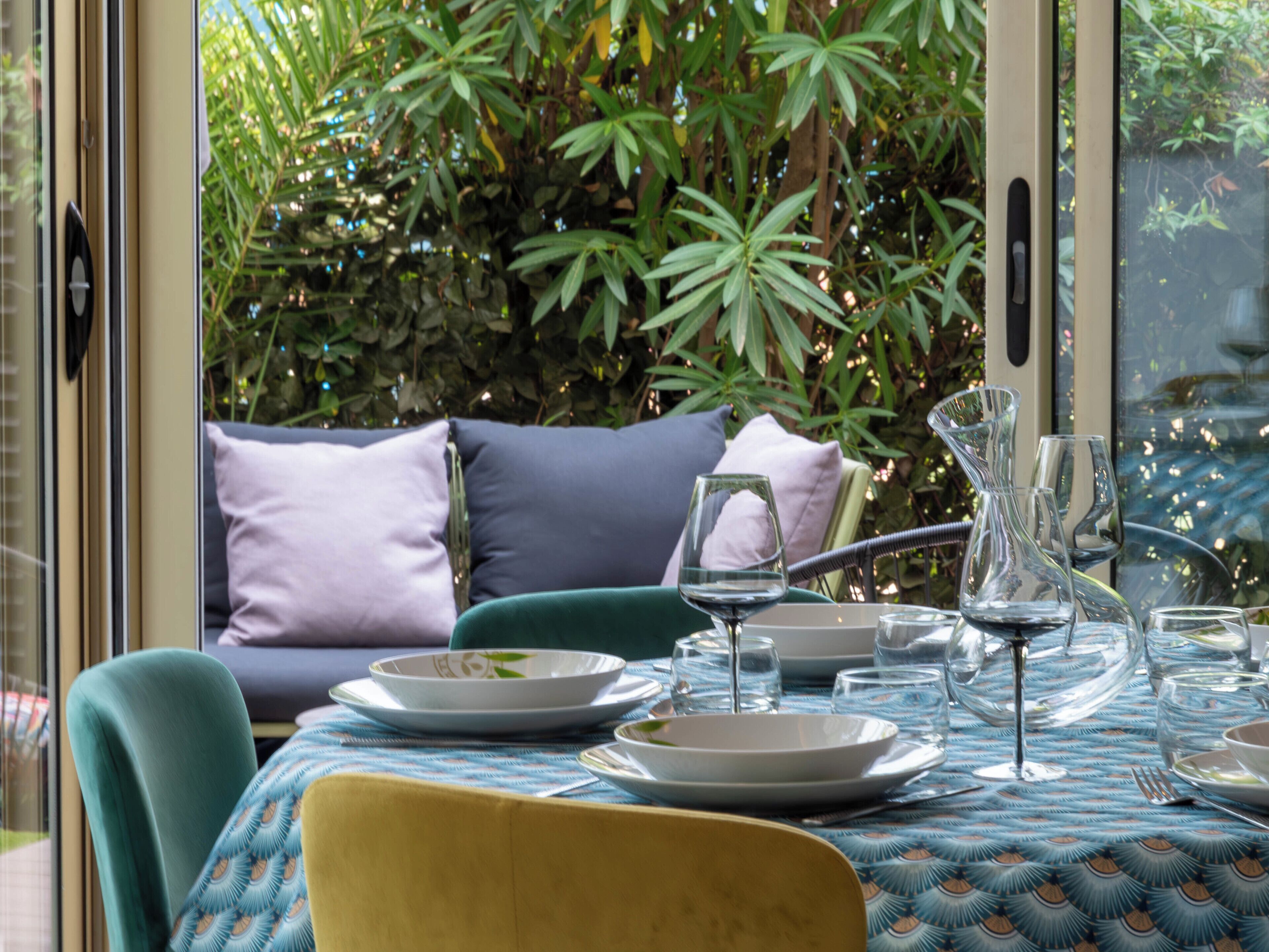 Un espace extérieur aménagé pour prendre les repas, avec une table dressée pour deux personnes, entourée de verdure.