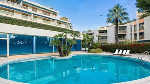 A swimming pool with lounge chairs, palm trees, and a multi-story building with balconies.