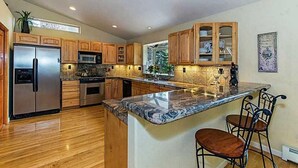 A modern kitchen with wooden cabinets, stainless steel appliances, and a marble island with bar stools. - Relaxing, Spacious 5-bedroom Tahoe Home Monthly Rental (Incline Village)