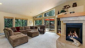 A spacious living room with a sectional sofa, a fireplace, and large windows offering a view of the outdoors. - Relaxing, Spacious 5-bedroom Tahoe Home Monthly Rental (Incline Village)