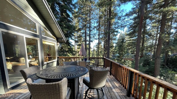 A wooden deck with wicker furniture and a glass door leading to a room with a bed and a chair. - Relaxing, Spacious 5-bedroom Tahoe Home Monthly Rental (Incline Village)