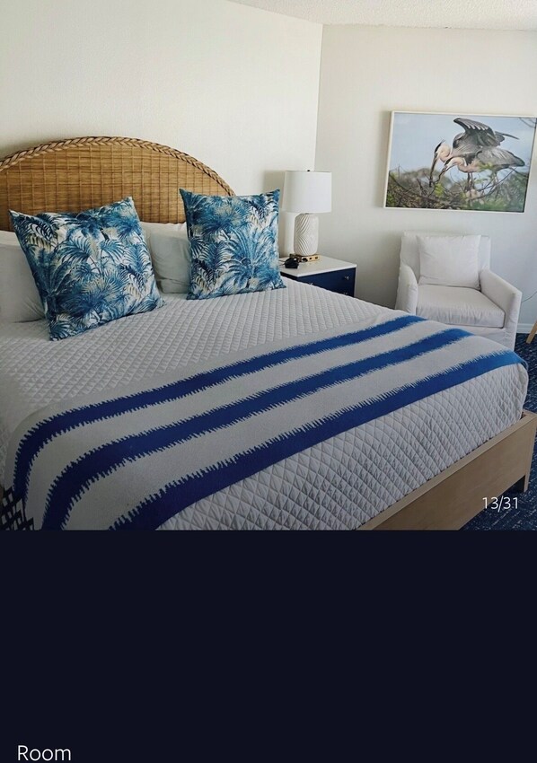 A hotel room with a bed, two pillows, a nightstand, a lamp, a chair, and a framed picture on the wall.