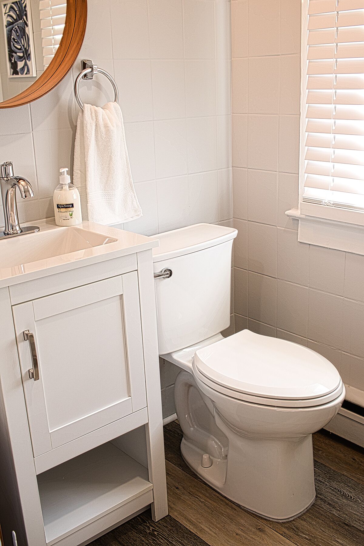 Un baño con inodoro blanco, un lavabo con espejo y una botella de jabón.