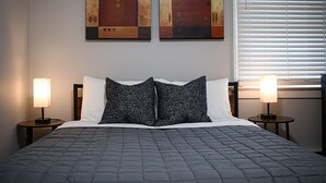 Un letto rifatto con copriletto trapuntato, due lampade sui comodini e due quadri astratti appesi al muro.
