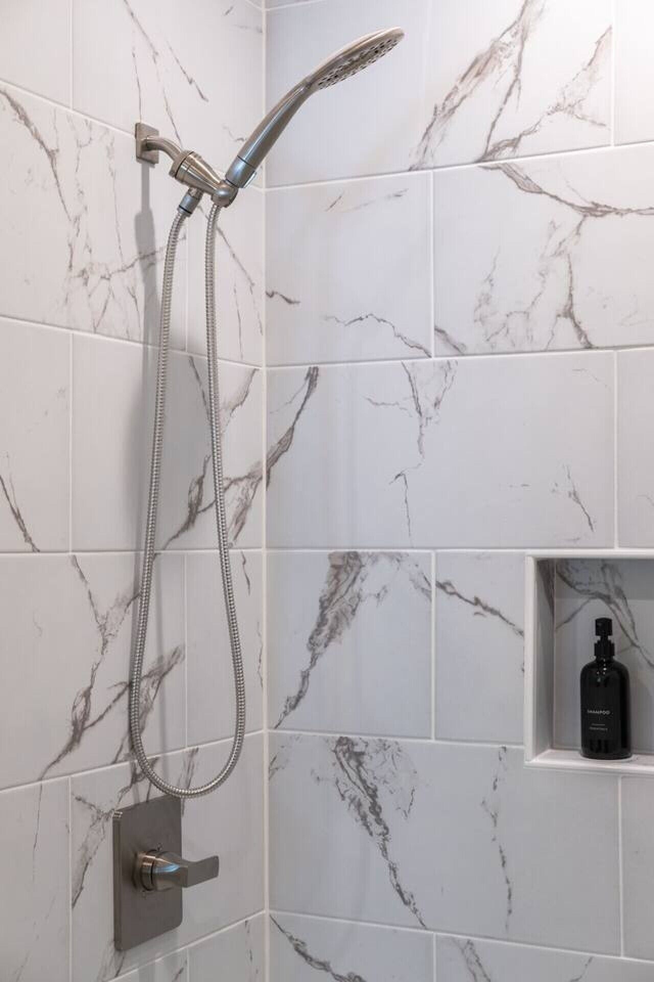 A shower with a handheld showerhead and a wall-mounted control.