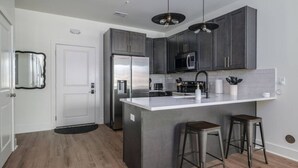 A modern kitchen with dark cabinets, a white countertop, and two bar stools. - Fabulous Flat in Trussville! (Trussville)