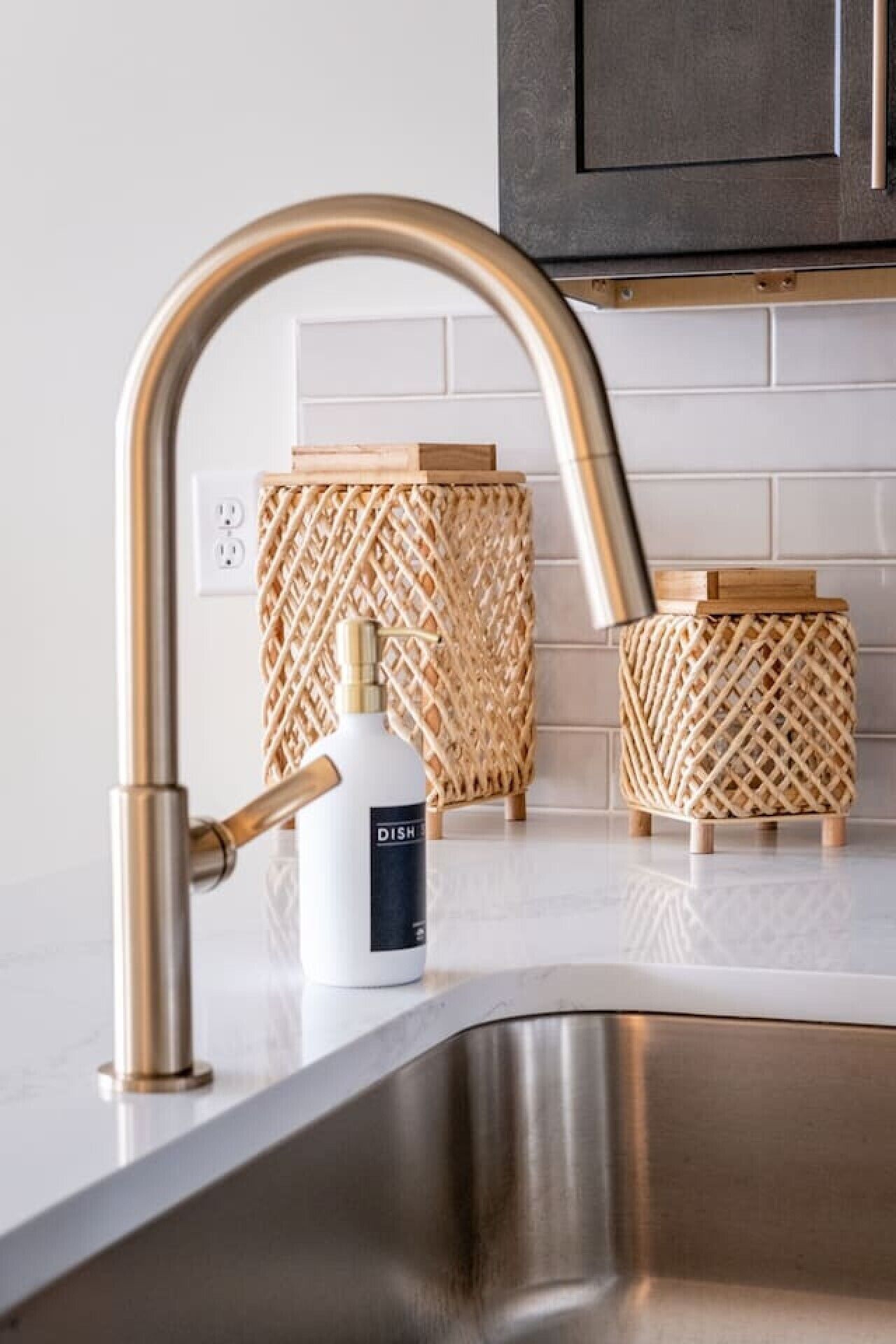 A kitchen with a stainless steel sink, a gold faucet, and two woven wooden stools.