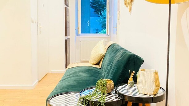 A room with a green sofa, a small side table, a lamp, and a window with a view of greenery. - Ottakring Gem/Cozy Room /w Breathtaking City Views (Vienna)