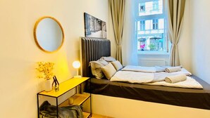 A bedroom with a bed, a bedside table with a lamp, a mirror, and a window with curtains. - Ottakring Gem/Cozy Room /w Breathtaking City Views (Vienna)