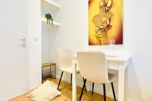 A modern room with a white desk, two chairs, a mirror with lights, and a framed artwork on the wall.