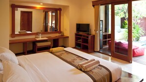 Une chambre d’hôtel comprenant un lit, un bureau avec une télévision, un miroir et une porte-fenêtre coulissante donnant sur un espace extérieur.