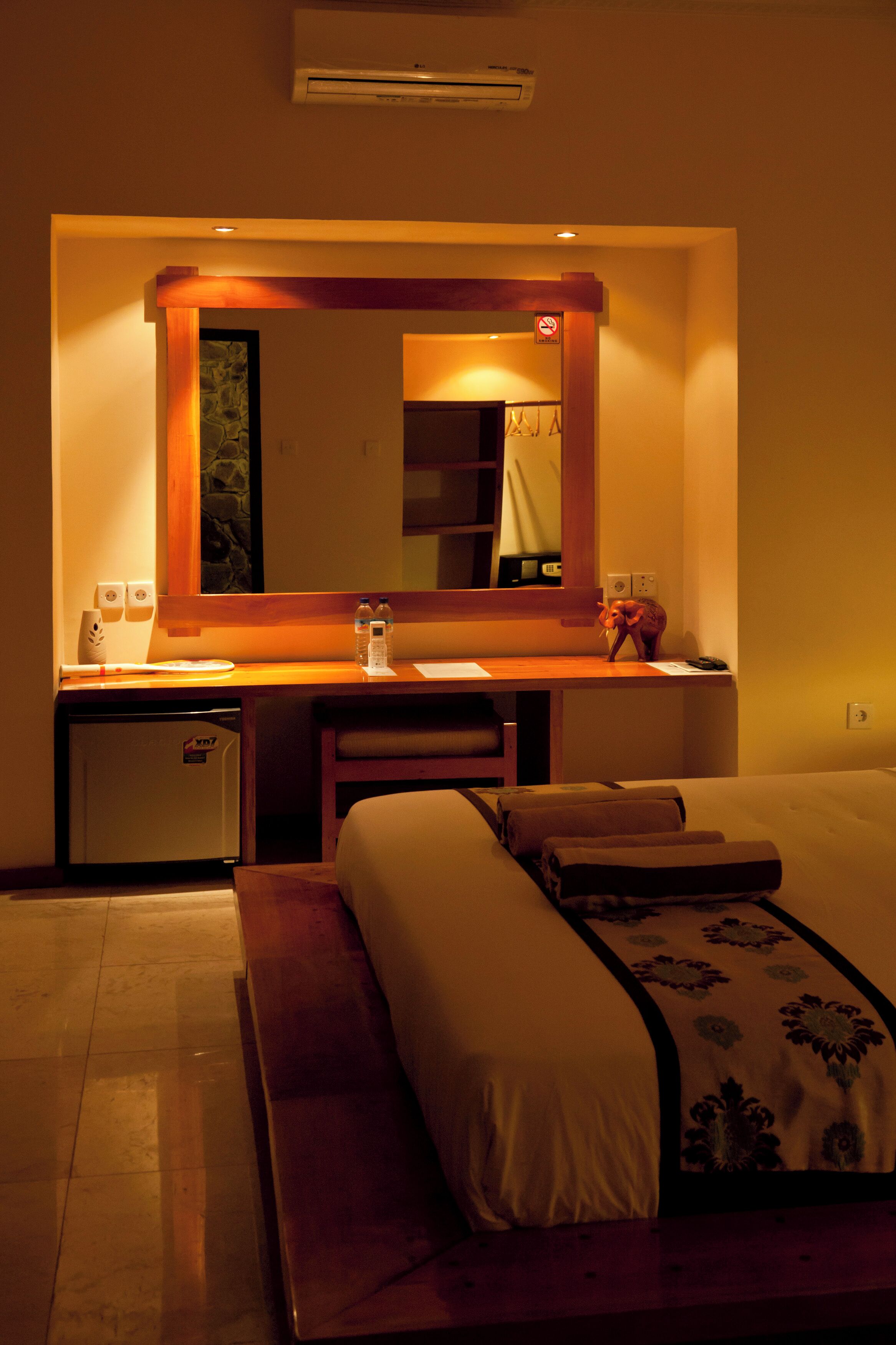 Une chambre d’hôtel comprenant un lit, une table de chevet, un miroir, un petit bureau et un climatiseur fixé au mur.