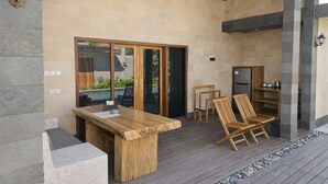 Un espace extérieur abrité, doté d’une table et de chaises en bois, de murs en pierre et d’une piscine visible à travers des portes vitrées.